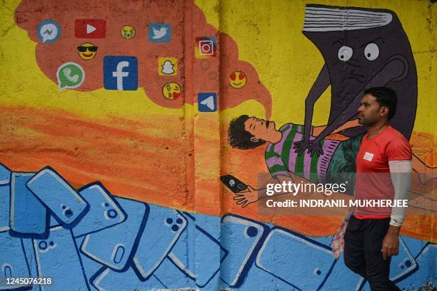 Man walks past a satirical wall mural portraying a teenager affected by social media addiction, in Mumbai on November 25, 2022.