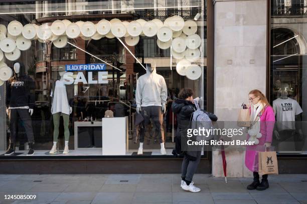 Shoppers walk past a window display that promotes Black Friday discounts in the windows of a retailer on Regent Street, on Friday 25th November 2022,...
