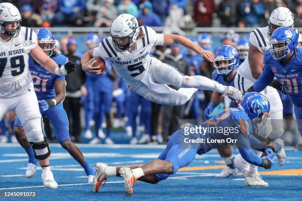 Quarterback Cooper Legas of the Utah State Aggies takes to the air to avoid the tackle of safety Seyi Oladipo of the Boise State Broncos during...