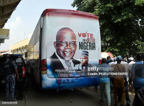 Members of the public stand behind a campaign poster of presidential candidate of All Progressives Congress Bola Tinubu and runningmate Abdullahi...