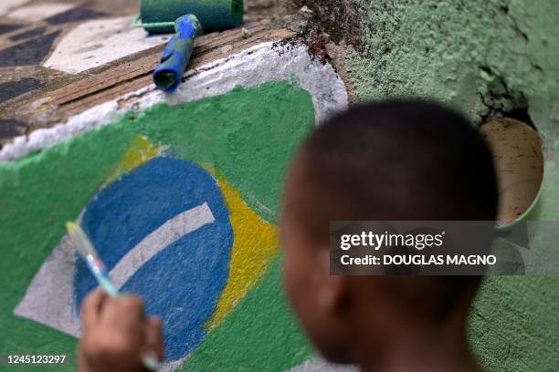 Child paints the Brazilian flag on a wall during an artistic intervention in Belo Horizonte, state of Minas Gerais, Brazil, on November 26, 2022. -...