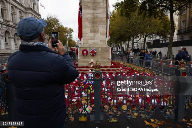 Man takes a photo of the Remembrance Sunday wreaths and poppies displayed at the Cenotaph in London.