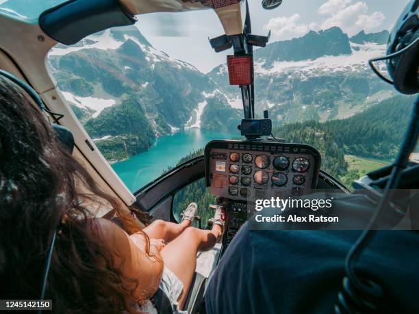 cockpit view of young women and male fly over glacier fed mountain lake in a helicopter - helicopter stock-fotos und bilder