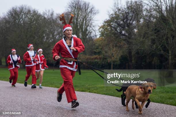 Fundraiser dressed as Santa Claus and wearing reindeer antlers runs alongside her dogs in the 2022 Windsor Santa Dash on the Long Walk in Windsor...