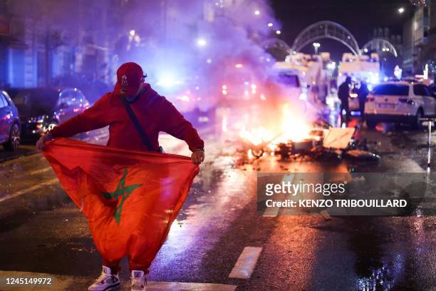 Fan holds a Moroccan flag as electric scooters burn in the back on the sideline of the live broadcast of the Qatar 2022 World Cup Group F football...