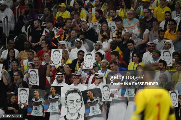 People on the stands hold portraits of German football player Mesut Ozil during the Qatar 2022 World Cup Group E football match between Spain and...