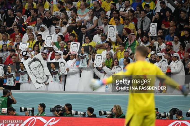 People on the stands hold portraits of German football player Mesut Ozil during the Qatar 2022 World Cup Group E football match between Spain and...