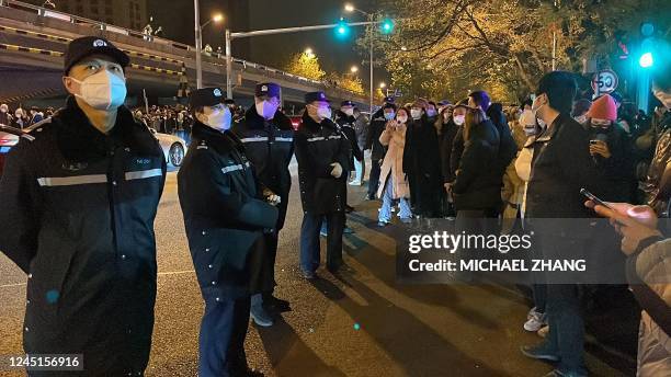 Policemen watch over protesters gathering along a street during a rally for the victims of a deadly fire as well as a protest against China's harsh...