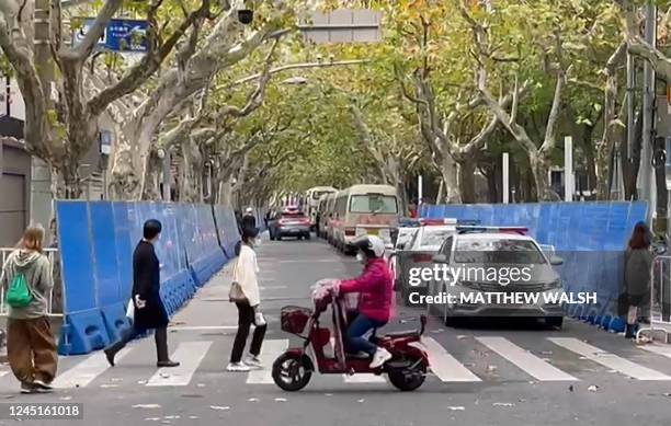 This frame grab from AFPTV video footage shows people walking past barricades and police presence on Wulumuqi street, named for Urumqi in Mandarin,...