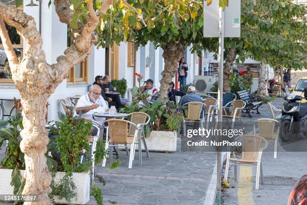 People at a coffee in Ikaria island. Sunny autumn day in Evdilos Village in Ikaria. Panoramic view of the traditional picturesque fishing village...