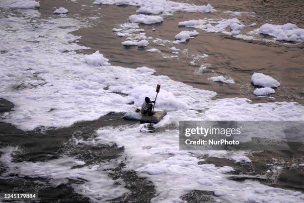 Man rows a makeshift boat as he looks for recyclables in the polluted waters of river Yamuna laden with toxic foam in New Delhi, India on November 6,...