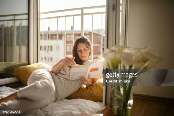 giovane donna che legge libro a letto a casa - leggere foto e immagini stock