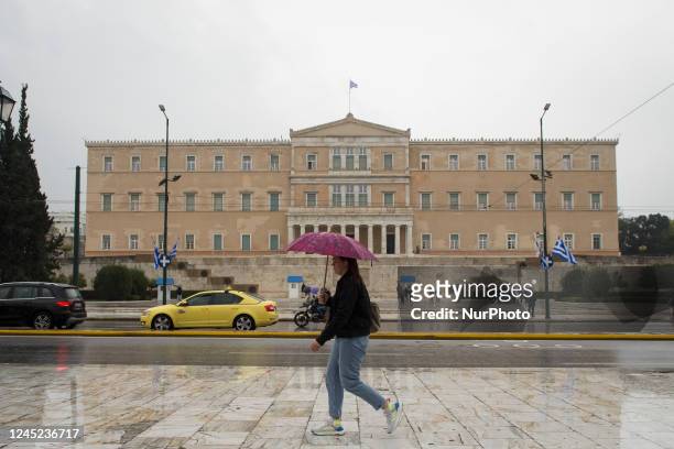Woman holding umbrella is passing in front of the Greek Parliament during a rainy day in Athens, Greece on November 30, 2022.