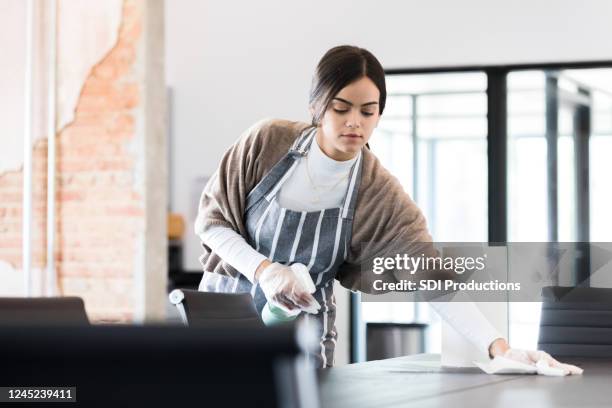 young woman uses protective gloves and disinfecting spray to clean - office cleaning stock pictures, royalty-free photos & images