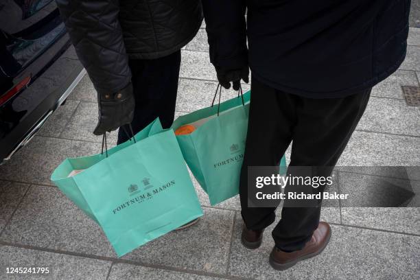 Two male shoppers stand holding the famous green shopping bags from Fortnum & Mason, on 29th November 2022, in London, England.