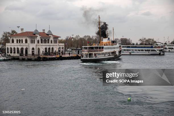 City lines ferry approaching the pier while emitting smoke during a cloudy day in Istanbul.