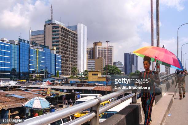 Pedestrian shelters from the sun under an umbrella in the Lagos Island district of Lagos, Nigeria, on Monday, Nov. 14, 2022. Nigeria's economy grew...