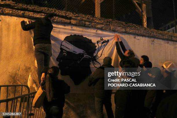 People hang up a Corsican flag on a wall as they take part in a demonstration outside Ajaccio's police station to protest against the arrests of...
