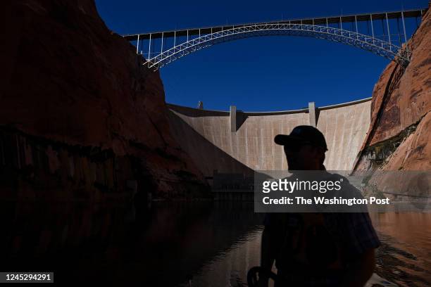 United States Geological Survey Research Ecologist Ted Kennedy drives his boat along the Colorado River as the The Glen Canyon Dam is seen in the...