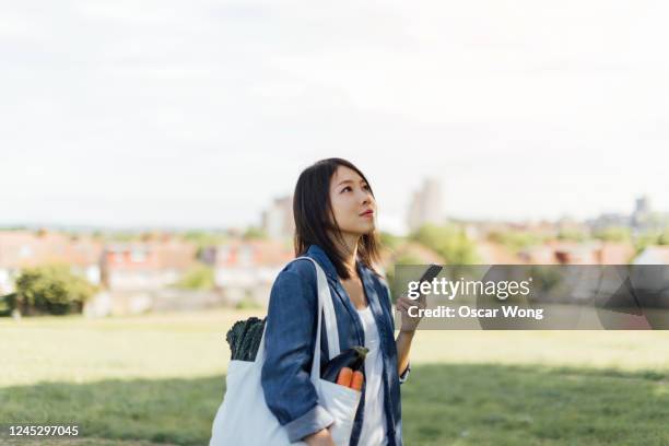 young woman with reusable shopping bag relaxing at the park - europe asian culture stockfoto's en -beelden