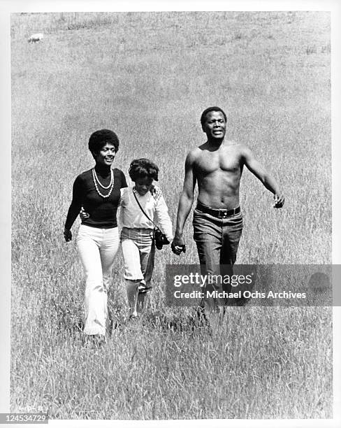 Esther Anderson, Yvette Curtis and Sidney Poitier walking through a field in a scene from the film 'A Warm December', 1973.