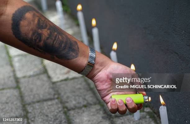 Fan of Santos with his arm tattooed with an image of Brazilian football legend Pele lights candles during a vigil outside the Albert Einstein...