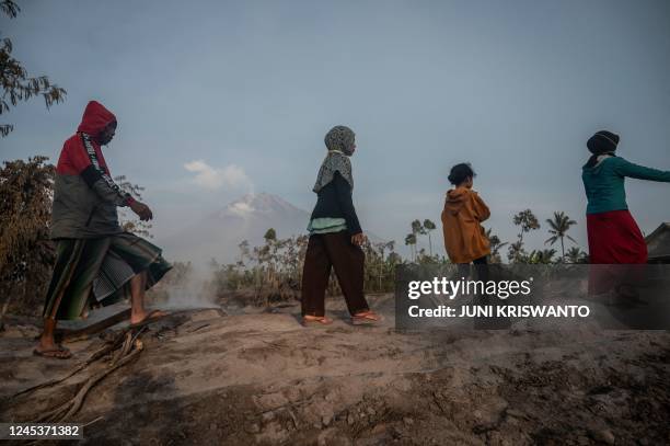 People walk before Mount Semeru following a volcanic eruption at Kajar Kuning village in Lumajang on December 5, 2022. - Indonesia's Mount Semeru...