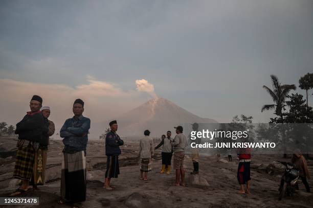 People stand before Mount Semeru following a volcanic eruption at Kajar Kuning village in Lumajang on December 5, 2022. - Indonesia's Mount Semeru...
