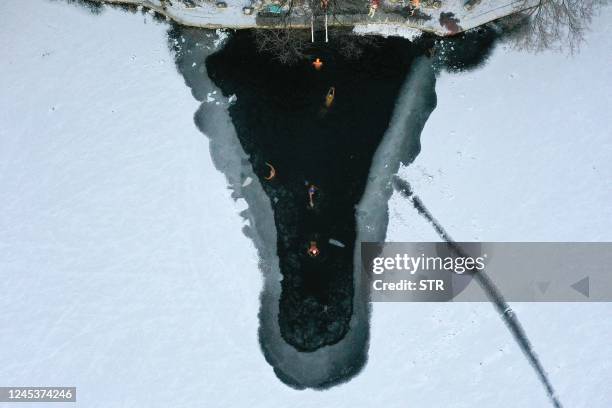 This aerial photo taken on December 3, 2022 shows winter swimming enthusiasts swimming in a partly frozen lake after snowfall in Shenyang, in...