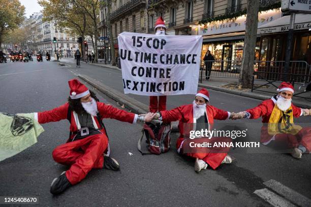 Man holds a banner reading "15th COP, last chance against extinction" as "Extinction Rebellion" activists dressed as Santa Claus sit on the Boulevard...