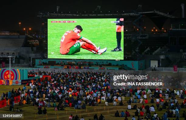 Qatar's migrant workers watch the Qatar 2022 World Cup round of 16 football match between Morocco and Spain with Moroccos defender Nayef Aguerd on...