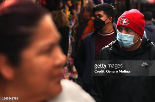 Shoppers, some wearing masks, some not, make their way along Santee Alley in Los Angeles on December 6, 2022. Los Angeles County appears in the midst...