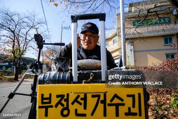 This photo taken on November 16 shows protester Ryu Guk-hyun using a suitcase to which he has attached a placard to support his lunch plate, as he...