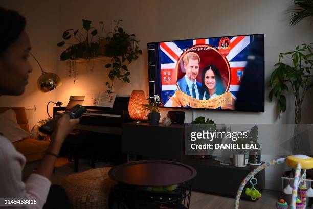 Woman poses as she watches an episode of the newly released Netflix docuseries "Harry and Meghan" about Britain's Prince Harry, Duke of Sussex, and...