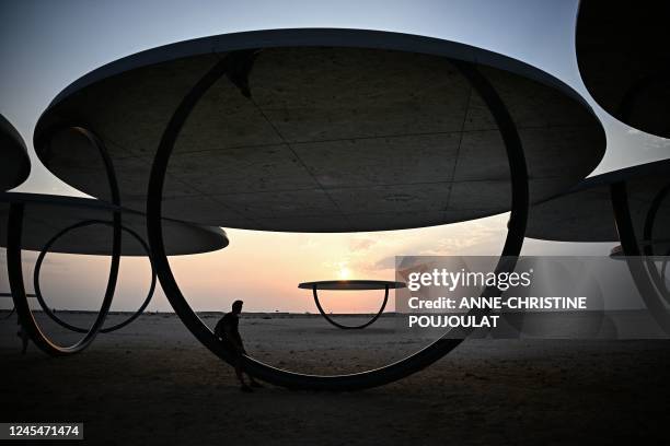 Man watches the sun set behind a large-scale installation by Icelandic-Danish artist Olafur Eliasson named "Shadows Travelling on the Sea of the Day"...