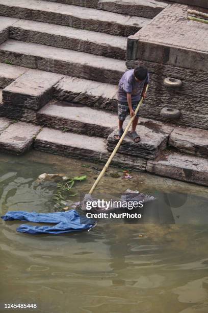 Young boy uses a bamboo pole to fish the clothing from a freshly cremated body out of the Bagmati River at Pashupatinath in Nepal. According to Hindu...