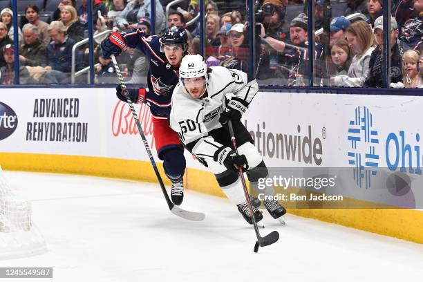 Sean Durzi of the Los Angeles Kings skates with the puck as Cole Sillinger of the Columbus Blue Jackets forechecks during the first period of a game...