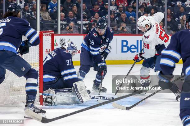 Goaltender Connor Hellebuyck of the Winnipeg Jets makes a stop as Aliaksei Protas of the Washington Capitals looks for the loose puck during first...