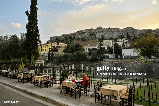 Tourists sit in an outdoor cafe-restaurant at the popular tourists Plaka area of Athens, before the sunset on December 8, 2022. - With most of...