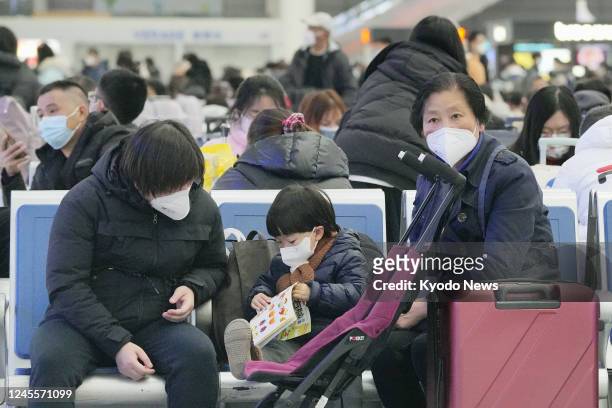 Passengers wearing face masks wait to board a train at a railway station in Shanghai on Dec. 12 as China faces new challenges after relaxing its...