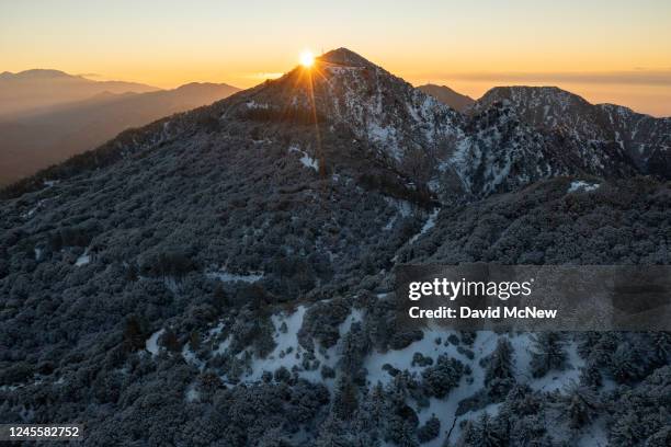 In an aerial view, cloudless weather at sunrise in the snow-covered San Gabriel Mountains is seen as a massive storm leaves California to spread...