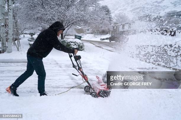 Man clears his driveway of snow from an overnight storm in Provo, Utah, on December 13, 2022. - A cross-country storm is expected to unleash blizzard...