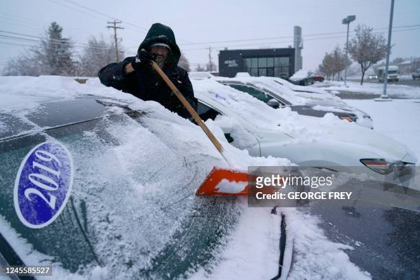 Worker clears cars of snow at the Bereg used car lot after an overnight storm in Orem, Utah on December 13, 2022. - A cross-country storm is expected...