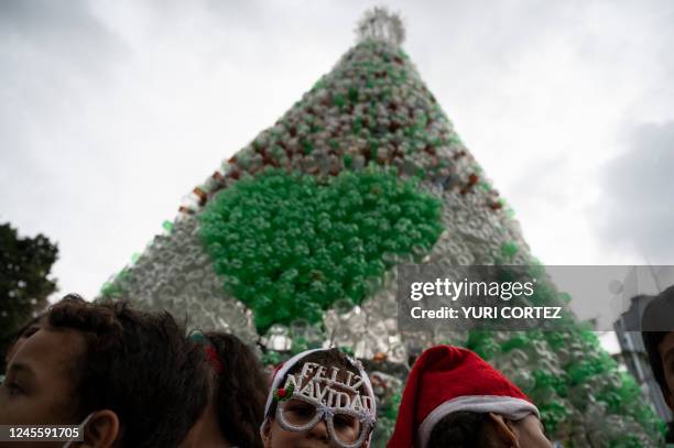 Children wearing Santa Claus' hats attend the lighting ceremony of a Christmas tree made from recycled plastic bottles by the non-profit and...