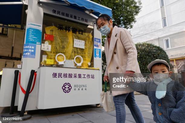 This photo taken on December 13, 2022 shows a woman and a child walking past a closed Covid testing booth in Shanghai. - China OUT / China OUT