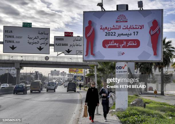 Woman and a girl walk along the side of a road underneath a billboard encouraging people to vote in the Tunisian national election scheduled for...