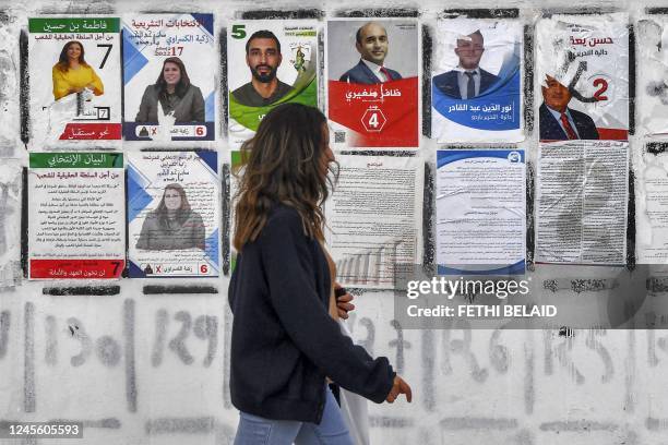 Youth walks past electoral posters for candidates running in the Tunisian national election scheduled for December 17, glued on a wall along the side...