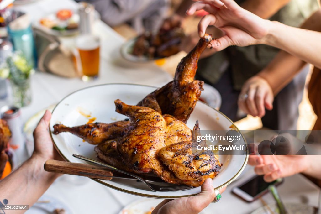 People grabbing chicken off the a serving plate at a family style wedding dinner.
