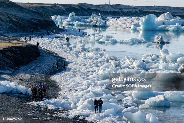 People are seen walking near the ice areas on the shore of Lake Jökulsárlón. Jökulsárlón is a lake in southern Iceland, with an area of 20 km2 and a...
