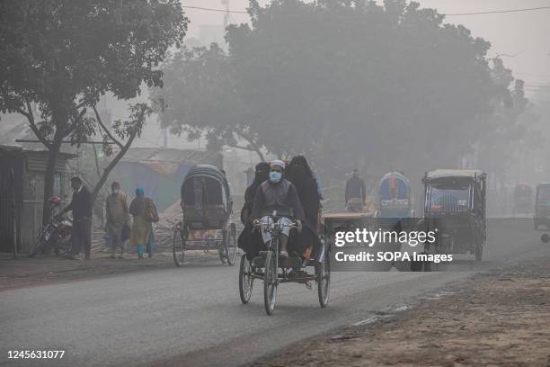 Rickshaw driver takes passengers to their destination on a foggy winter morning in Dhaka.